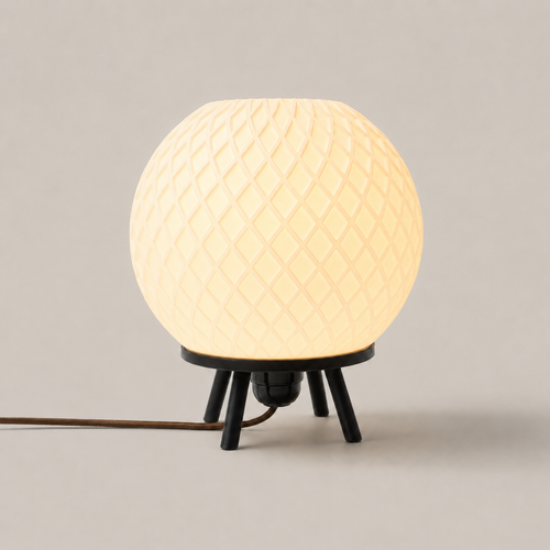 Quasar bedside lamp, a cream spherical shade with a diamond lattice texture on three black tripod legs, softly lit