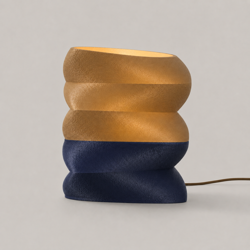 Zaha table lamp in amber and navy, a stacked rounded form with a matte textured surface, glowing from within
